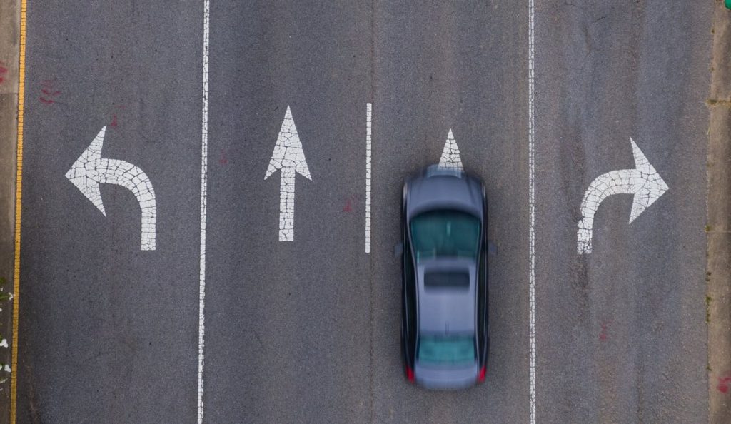 Tesla UK Sales 2026: Month-by-Month Tracker as at 15 Sep Top-down view of a moving car on a road with directional arrows, emphasizing urban transportation.
